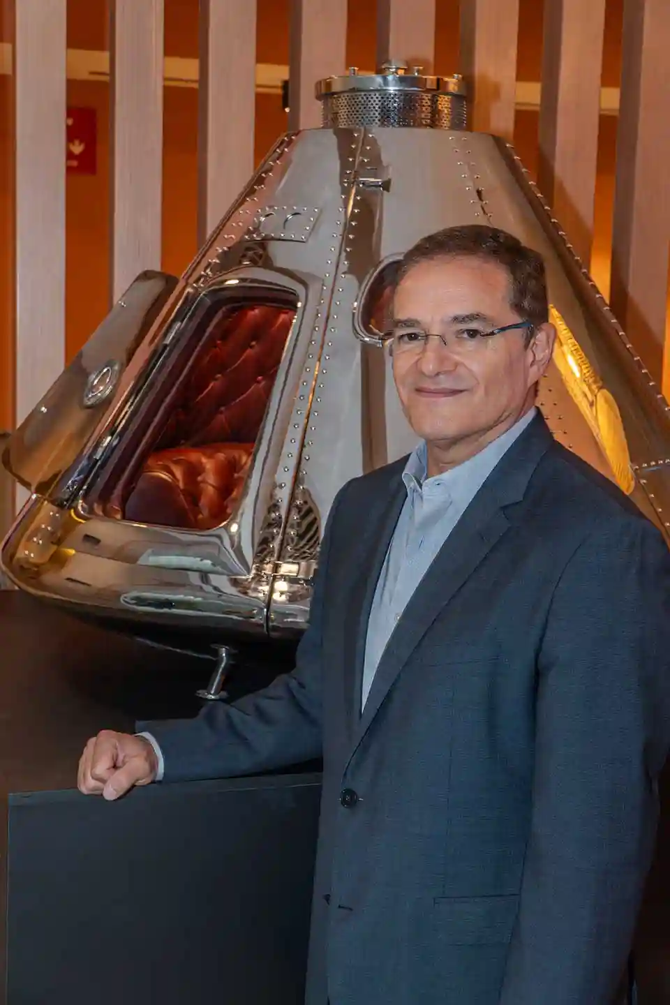 Man in suit standing beside a shiny metallic space capsule display.