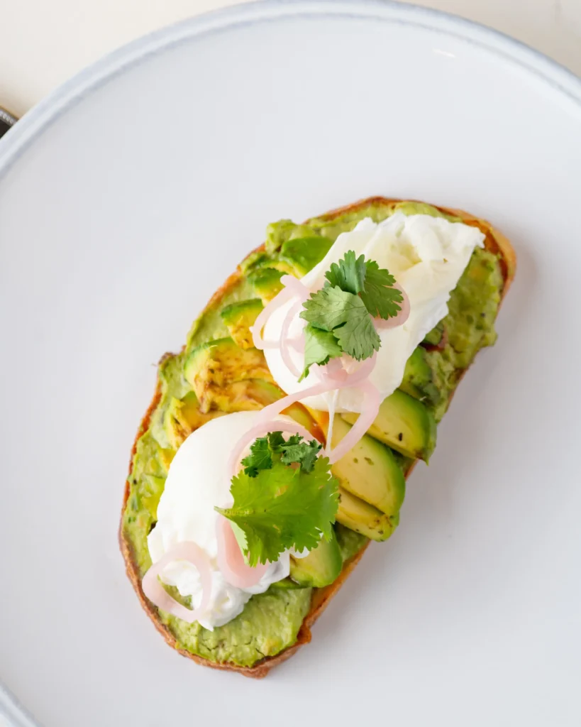 avocado toast topped with poached eggs, pickled onions, and fresh cilantro