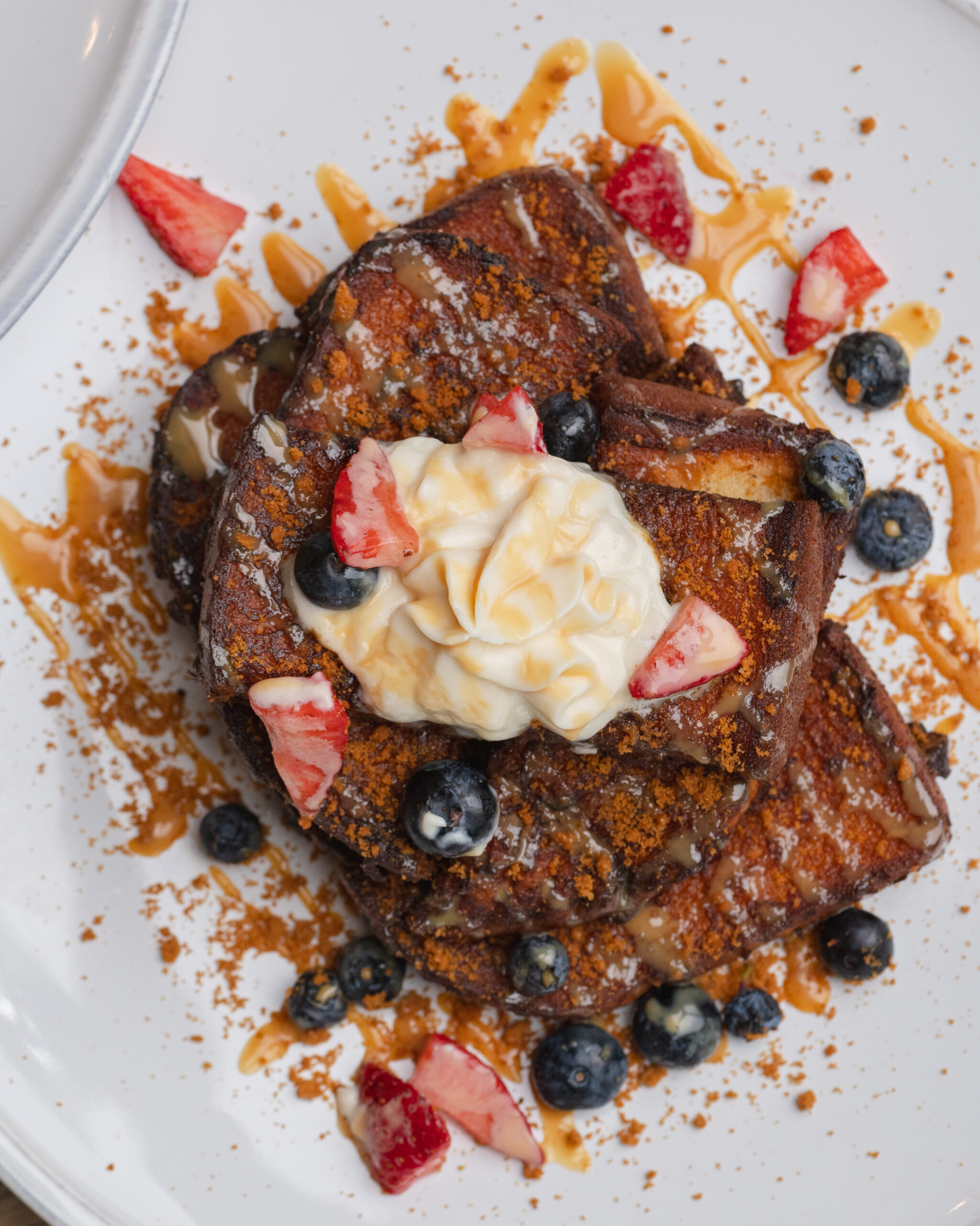 french toast topped with cream, strawberries, blueberries, and caramel drizzle
