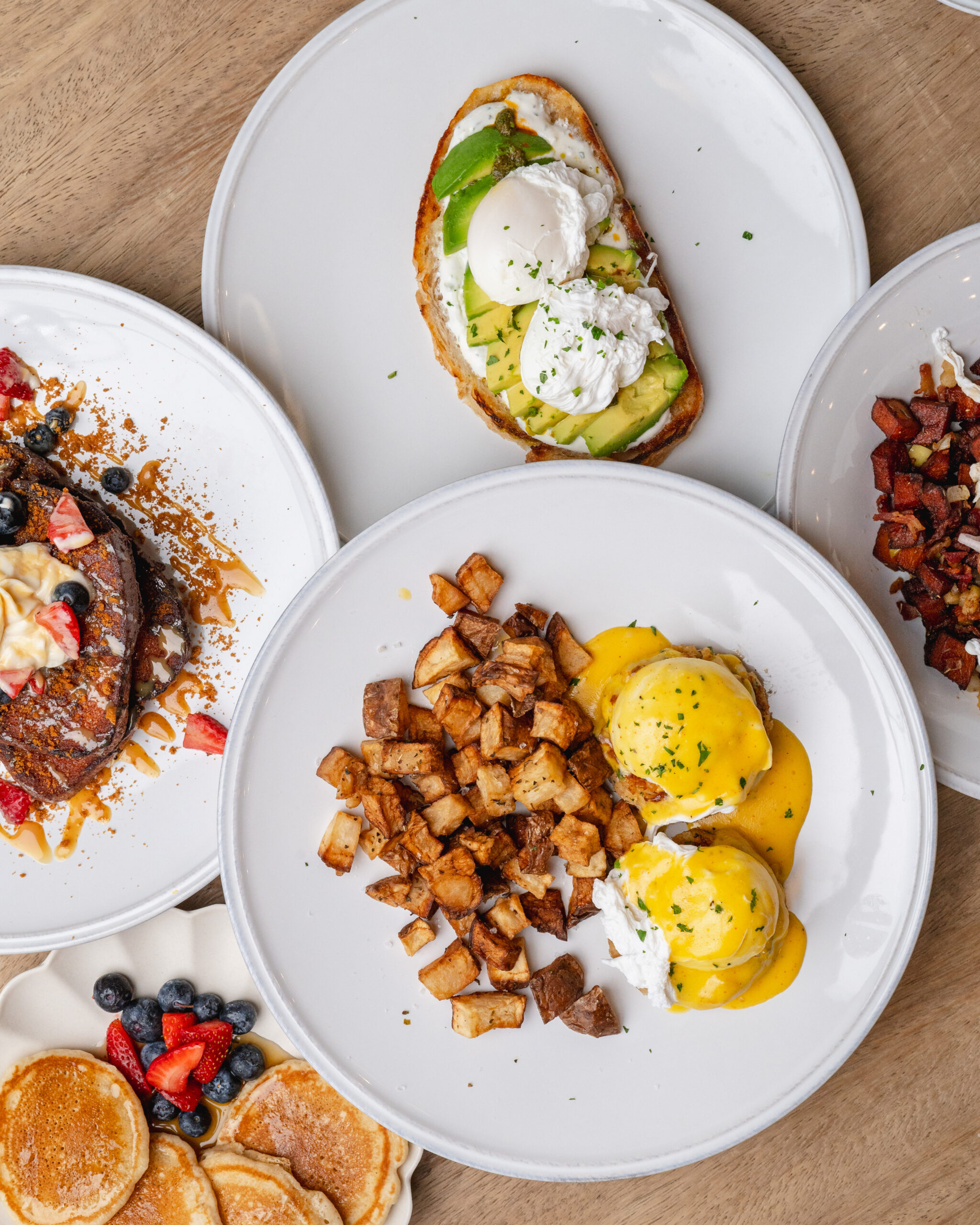 brunch spread featuring eggs benedict, avocado toast, pancakes, and potatoes