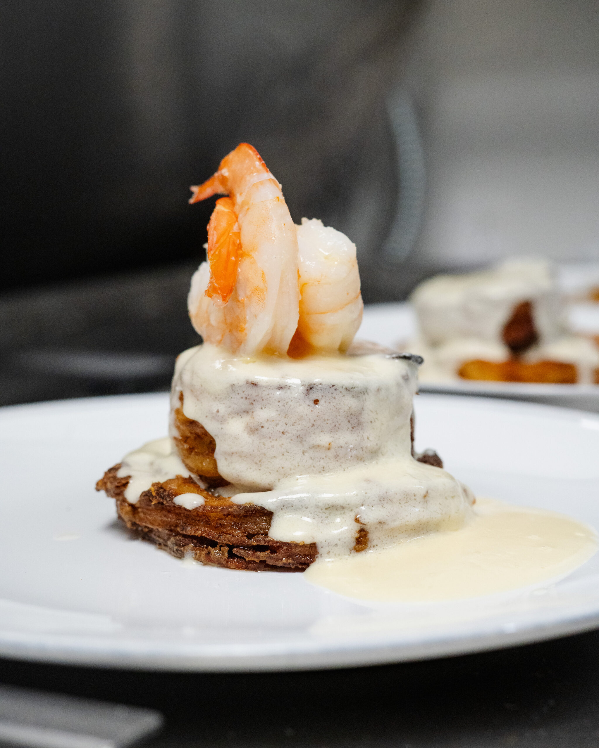 Shrimp-topped layered dish covered in creamy sauce on plate.