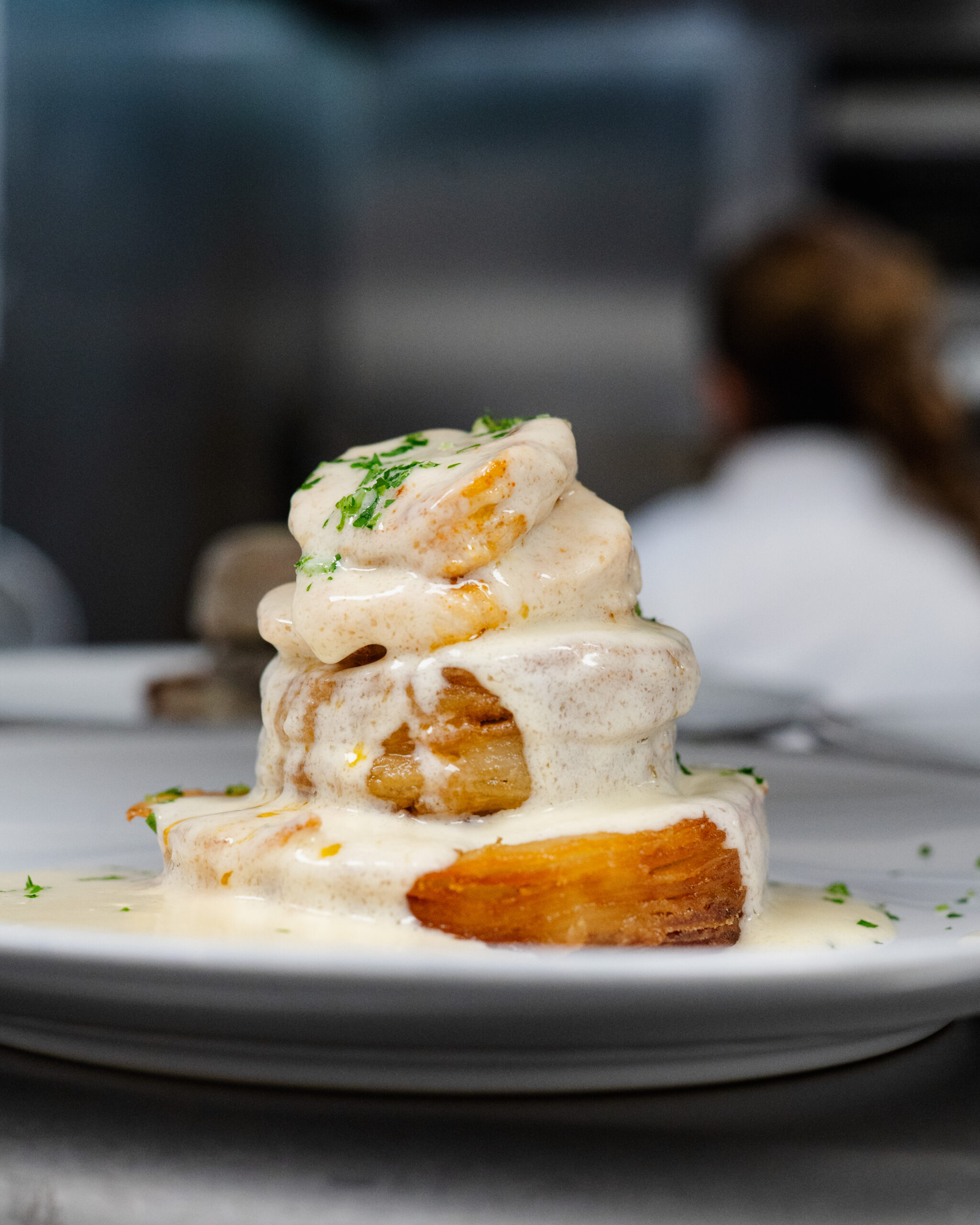Shrimp-topped layered dish covered in creamy sauce on plate.
