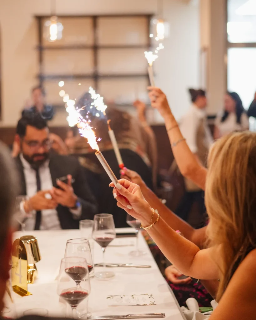 People holding sparklers while seated at festive dinner celebration.