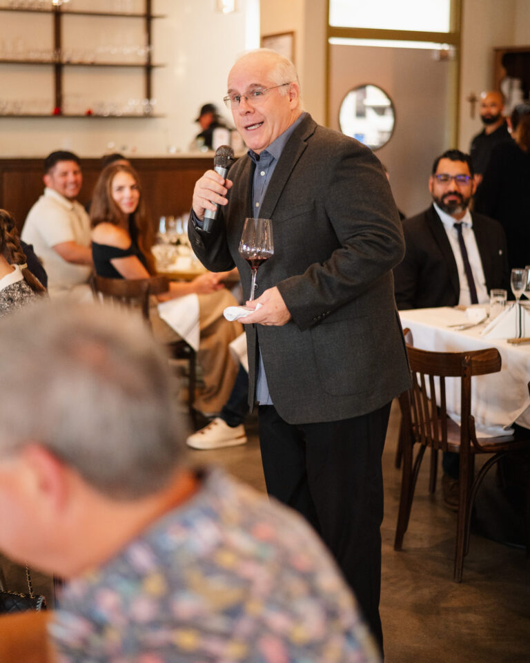 Man speaking into microphone holding wineglass during restaurant celebration.