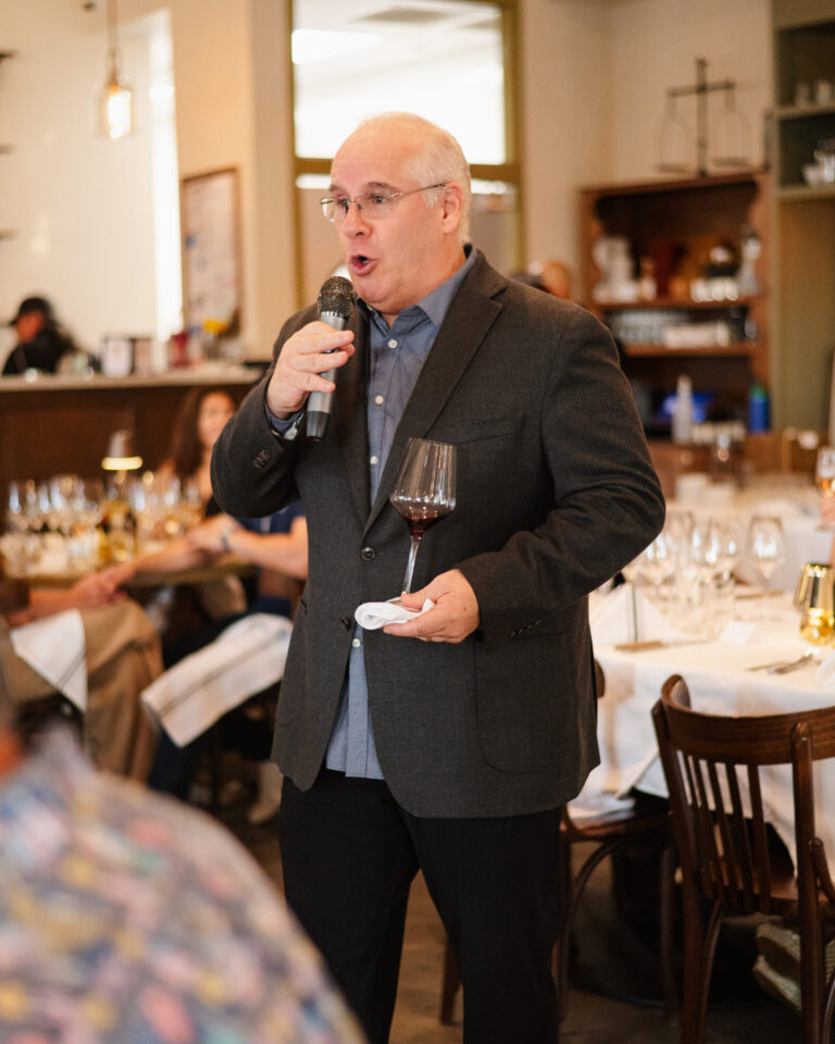 Man speaking into microphone holding wineglass during restaurant celebration.