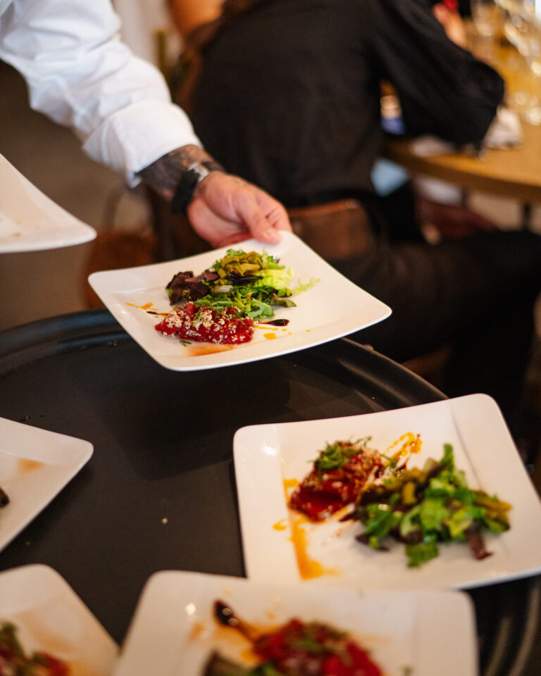 Waiter serving plated salads with greens and dressing at dinner.