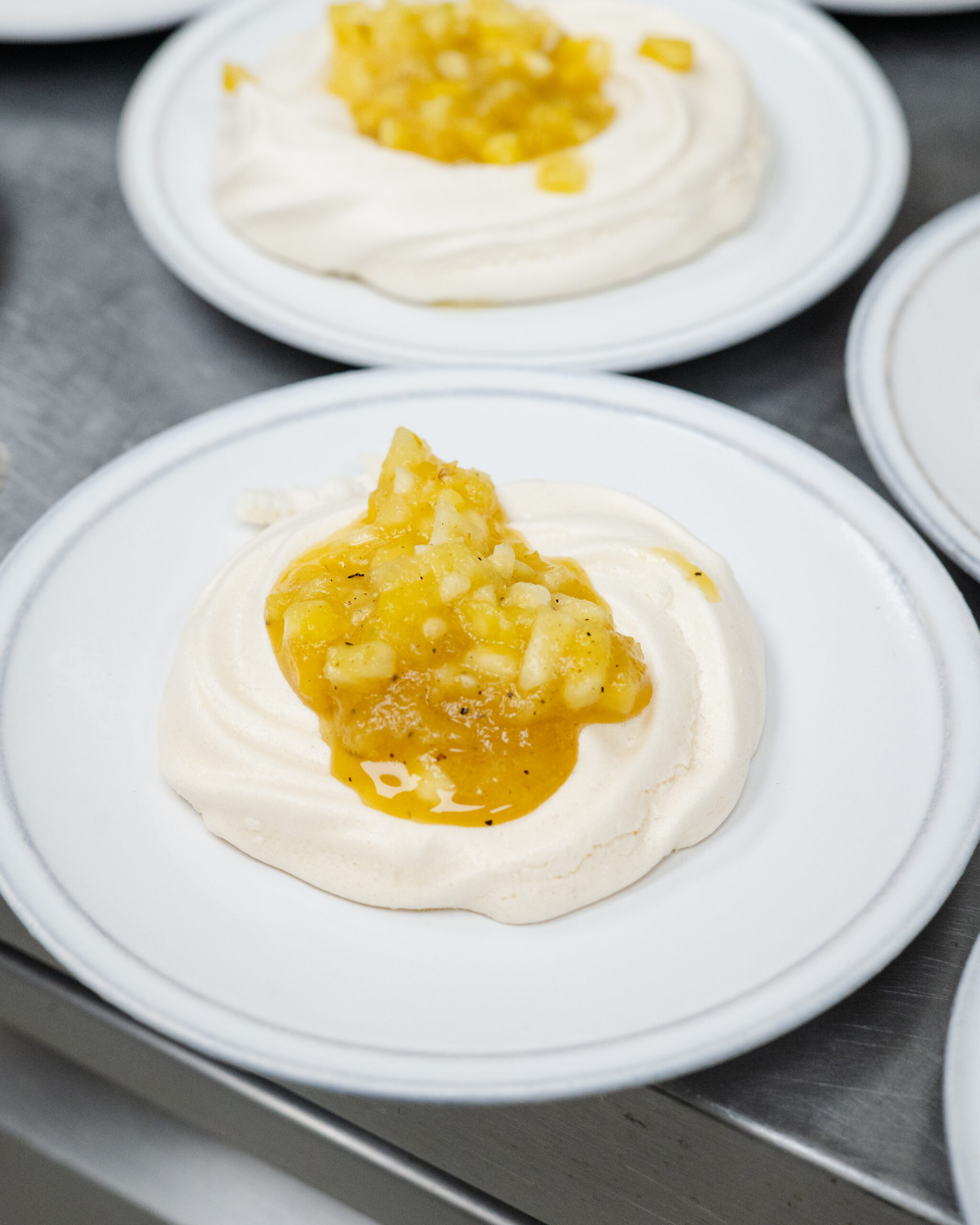 White dessert topped with diced pineapple and syrup on plate.