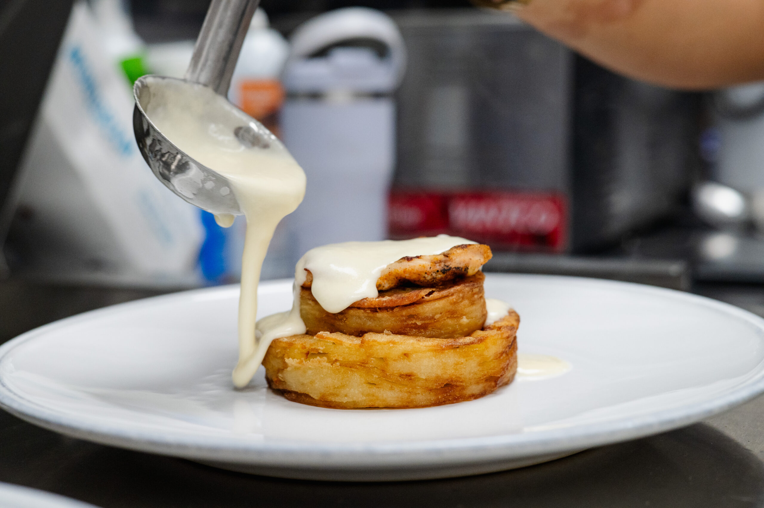 Sauce being poured over stacked pastry rounds on white plate.